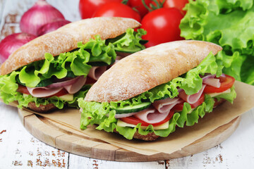 Two sandwiches with fresh vegetables, ham and cheese in ciabatta bread