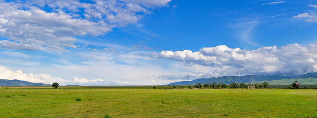 Panoramic view of the landscape in south eastern Kazakhstan under a blue sky with fluffy clouds.