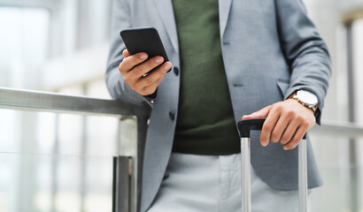 Unrecognizable businessman with luggage going on business trip, using smartphone.