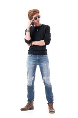 Displeased serious handsome redhead young stylish man talking on the cell phone looking away. Full length portrait isolated on white background. 