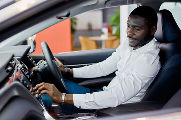 afro man sits inside of new automobile in dealership, examines it before making purchase. car, auto concept