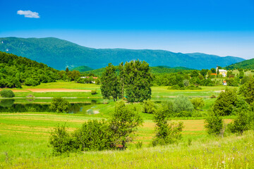 Fototapeta na wymiar Beautiful green landscape in Lika region Croatia, on Svica lake and mountains in background