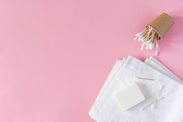 White towel with soap and wooden cotton swabs in an eco cup on a pink background, bath spa accessories