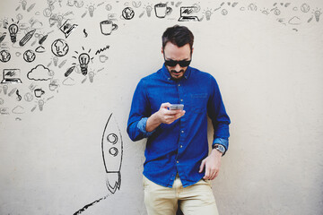 Bearded modern businessman browsing internet via mobile phone, hipster guy personalizing multimedia programs and applications on contemporary cell telephone while standing against copy space wall
