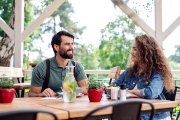 Happy couple sitting outdoors on terrace restaurant, talking.