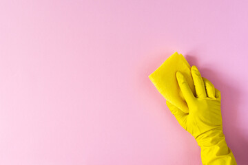 Hand in a yellow rubber glove with a cleaning sponge on a pink background