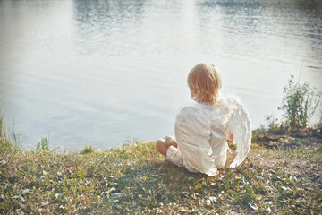 boy with wrings like an angel sitting on the bank of  river
