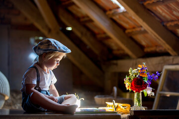 Cute beautiful child, blond kid, reading book and playing with construction blocks in a cozy attic...