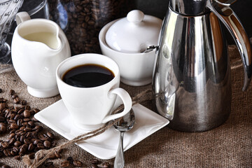 set table with a cup of filtered coffe with milk jug, coffe can and sugar jar