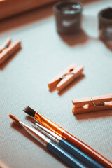 Three brushes of different shapes lie on a white canvas near paints and clothespins.