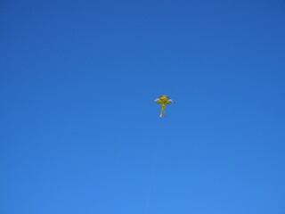 Child's toy kite in rainbow colors flying in a clear blue summer sky