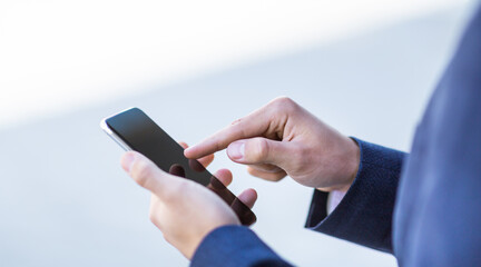 Closeup of corporate employee using internet on his cellphone outdoors, space for design