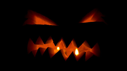 Fototapeta premium Halloween pumpkin with candles glowing inside at black background 