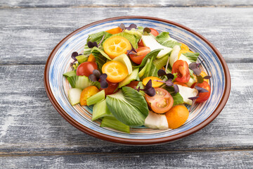 Vegetarian salad of pac choi cabbage, kiwi, tomatoes, kumquat, microgreen sprouts on gray wooden background. Side view.
