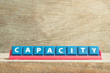 Tile letter on red rack in word capacity on wood background