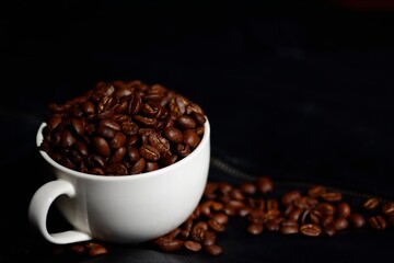Coffee beans and white mug isolated on black leather background.