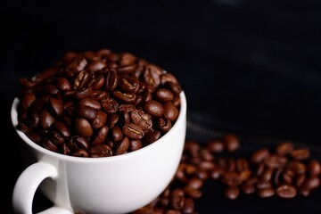 Coffee beans and white mug isolated on black leather background.