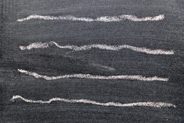 White color chalk hand drawing in set of wavy line shape on black board background