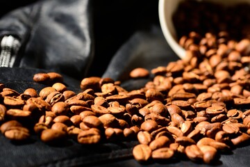 Coffee beans and white mug isolated on black leather background.