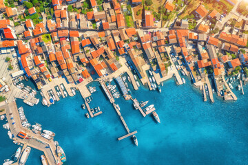 Fototapeta na wymiar Aerial view of boats and yachts in port in beautiful old city at sunset in Croatia in summer. Landscape with buildings with orange roofs, motorboats in harbor, clear blue sea, cars, road. Top view