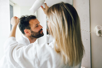 Close up of a playful woman blow drying her boyfriend's hair