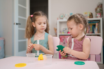 Obraz na płótnie Canvas Little girls with lovely faces play with clay molding shapes, learning through playing with colored plasticine developing creativity