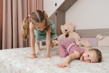 Happy funny little girls having fun on bed feeling joy, cheerful cute active kids having fun playing laughing in bedroom
