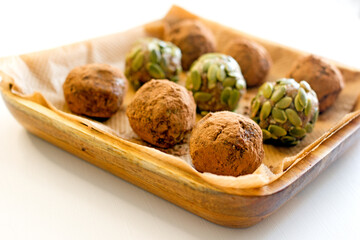 Homemade vegan candy balls from nuts, dates, seeds, cocoa free sugar on a wooden plate on a white background close-up. Energy balls, raw food dessert, copy space.The concept of healthy desserts