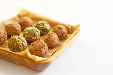 Homemade vegan candy balls from nuts, dates, seeds, cocoa free sugar on a wooden plate on a white background close-up. Energy balls, raw food dessert, copy space.The concept of healthy desserts