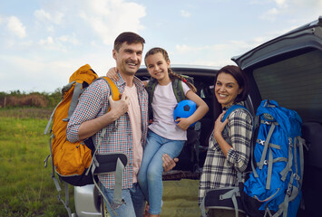 Smiling family of travelers by car standing in nature in summer.