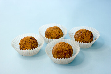 Sweet energy candy balls in white paper tins on a blue background. The concept of raw food desserts from dates, nuts, coconut, seeds, sugar and gluten free.