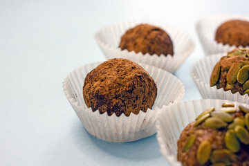 Sweet energy candy balls in white paper tins on a blue background. The concept of raw food desserts from dates, nuts, coconut, seeds, sugar and gluten free.