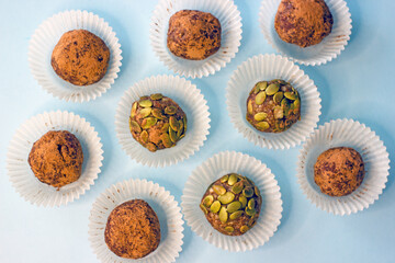 Sweet energy candy balls in white paper tins on a blue background. The concept of raw food desserts from dates, nuts, coconut, seeds, sugar and gluten free.