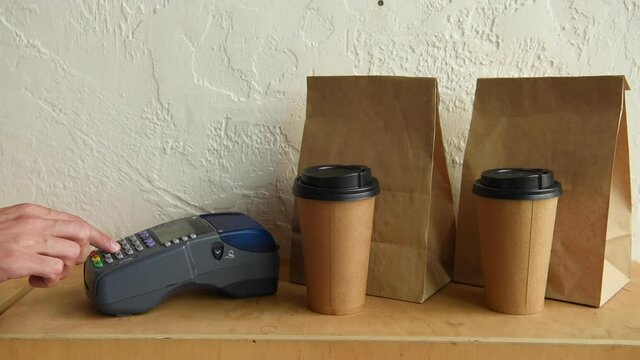 cropped view of man using payment terminal near paper bags and disposable cups
