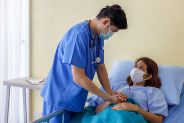 Fototapeta premium Asian male doctors wear uniforms and medical masks, holding hands with middle-aged female patients to encourage patients.
