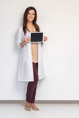 Portrait of smiling young doctor in white coat showing the screen of digital tablet in her hand.