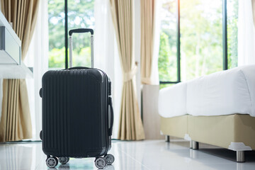 Black Luggage in modern hotel room with windows, curtains and bed against green nature background....