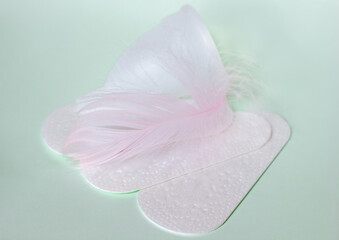 Sanitary pad, two menstrual cups and feather on a light green background