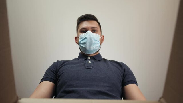 Coronavirus quarantine home isolation, man POV opening carton box delivery and pulling out gift purchase. Male in medical protection mask looking in box and happy to receiving products. courier e