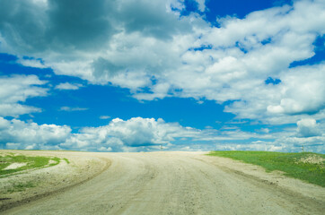 White stone road towards a bright blue sky with fluffy clouds rural landscape