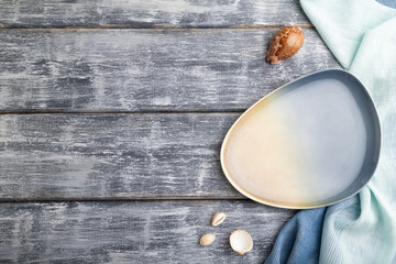 Empty blue ceramic plate on gray wooden background and blue textile. Top view, copy space.