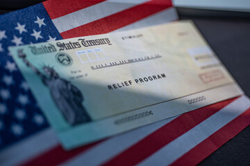COVID-19 economic Stimulus check on blurred USA flag and sun light background. Relief program concept.