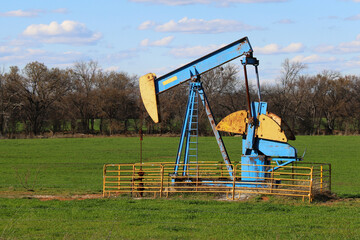 a rusted vintage bright painted old abandoned oil well derrick historic empty green meadow cow...