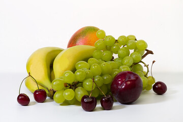 Fresh fruits in assortment. Bananas, grapes, mangoes, cherries, plums on a light background.
