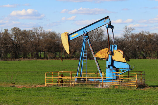 a rusted vintage bright painted old abandoned oil well derrick historic empty green meadow cow pasture rusty iron fence