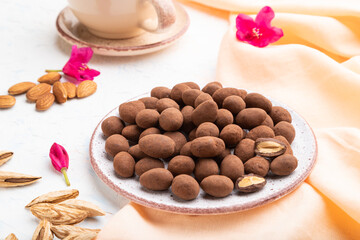 Almond in chocolate dragees on ceramic plate and a cup of coffee on white concrete background. Side view.