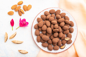 Almond in chocolate dragees on ceramic plate and a cup of coffee on white concrete background. Top view, close up.