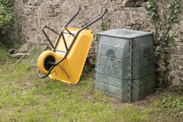 wheelbarrow and plastic compost bin in home garden in sunny day