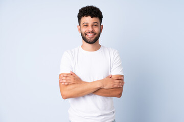 Young Moroccan man isolated on blue background with arms crossed and happy