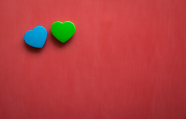 Fototapeta premium Two blue and green hearts lying close together isolated on right corner of red background. Flat lay with empty space for text.